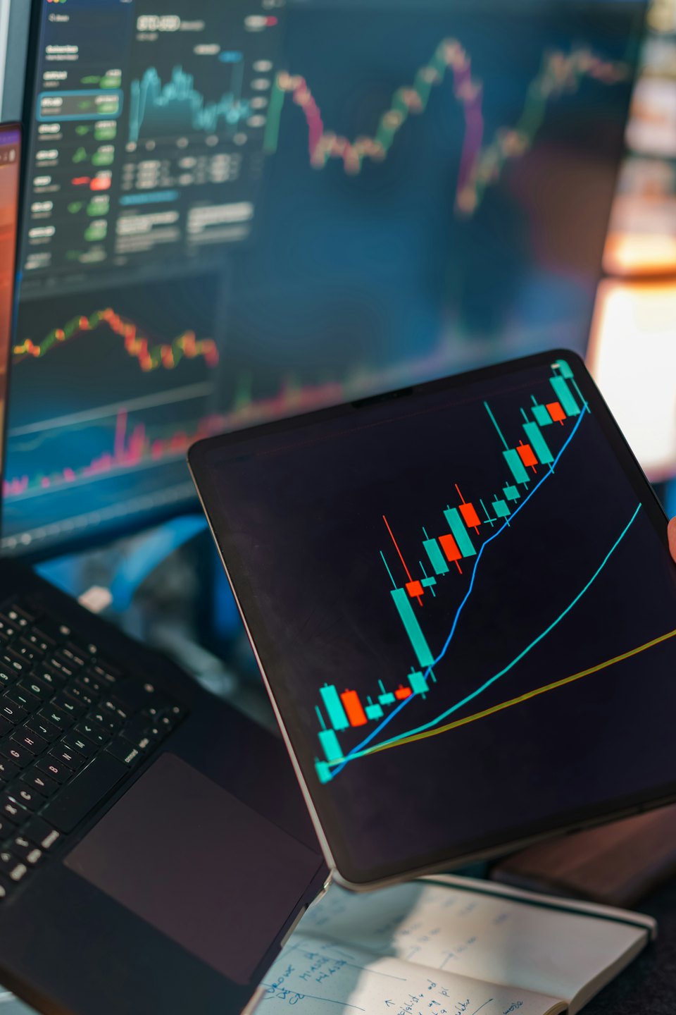 Hand holding a tablet showing a financial chart over a laptop.
